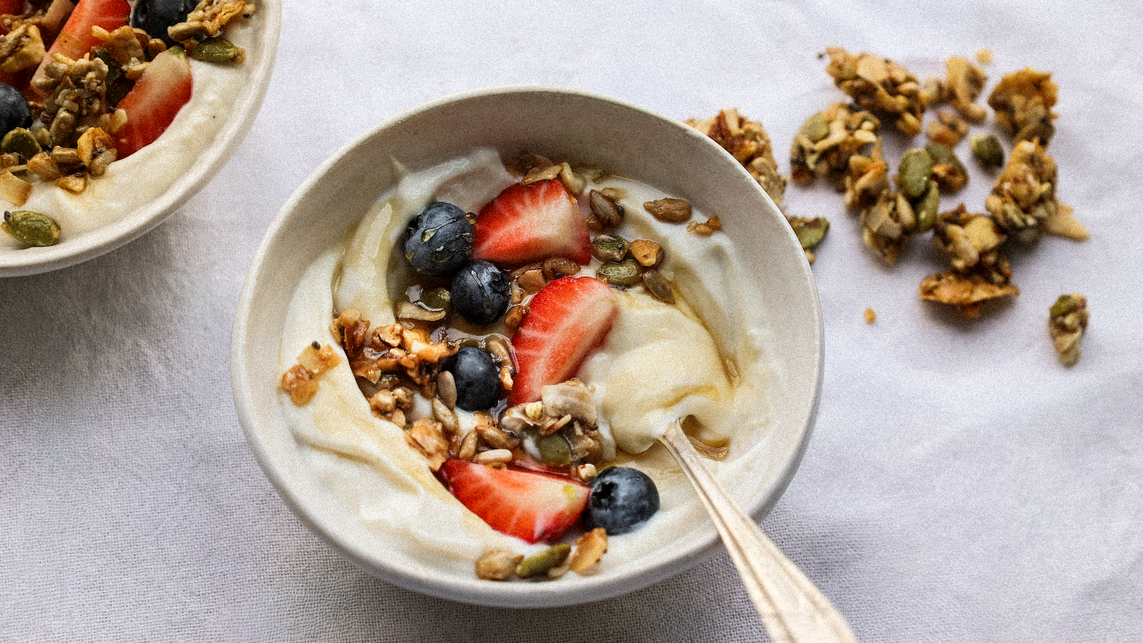 A bowl of yogurt topped with Hapüs Grain-Free Granola, honey, strawberries, and blueberries.